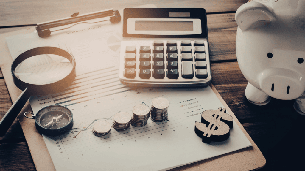 Calculadora, mealheiro, moedas empilhadas e gráfico de crescimento sobre secretária de madeira, simbolizando planeamento financeiro empresarial.